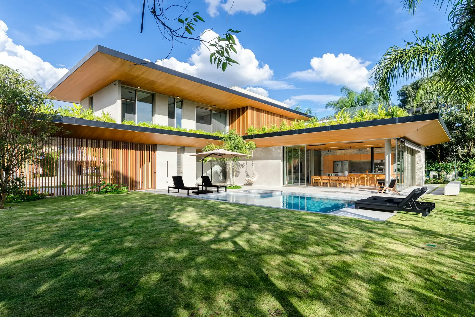 Rumah Kolam: a two-storey house with deep eaves, a lawn and a pool