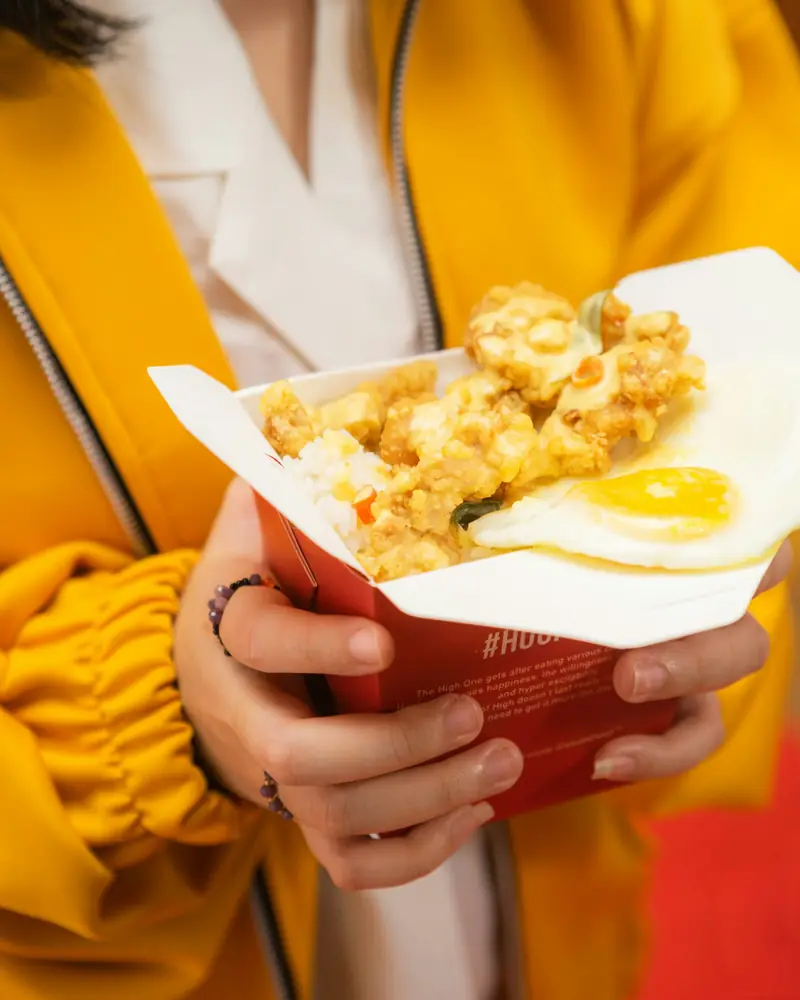 Hands holding a takeaway box of fried rice with an egg