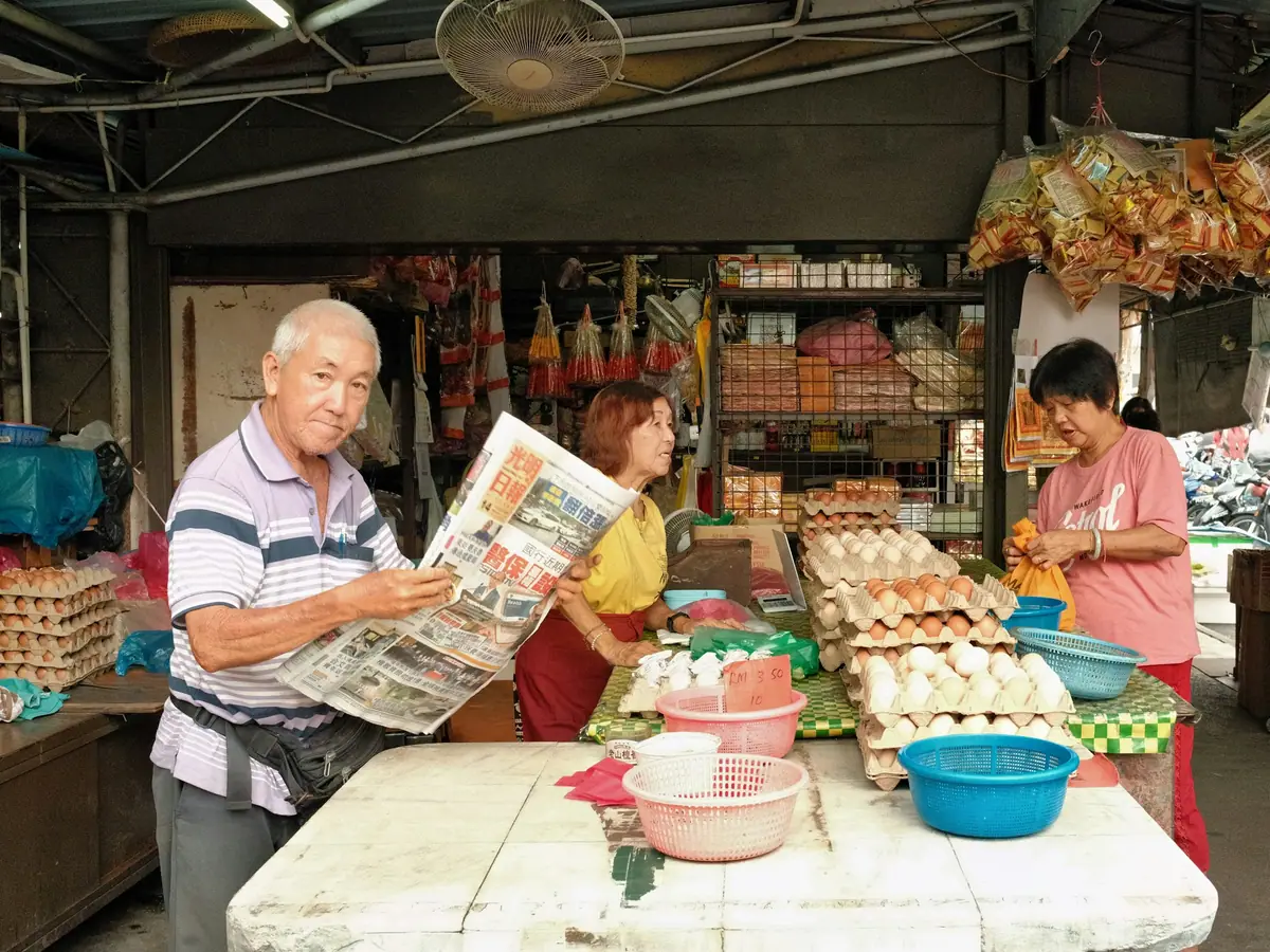 A shopkeeper reading the newspaper at his grocery stall