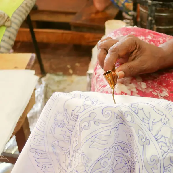 A hand tracing wax lines onto white cloth with a canting