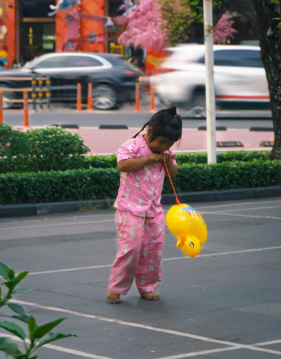A small child in pink pyjamas pulling a yellow duck toy