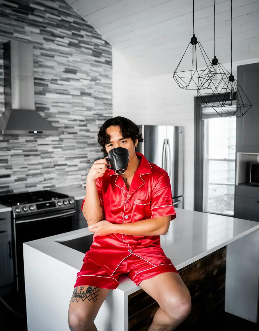 A man in a red satin short set drinking coffee in a kitchen