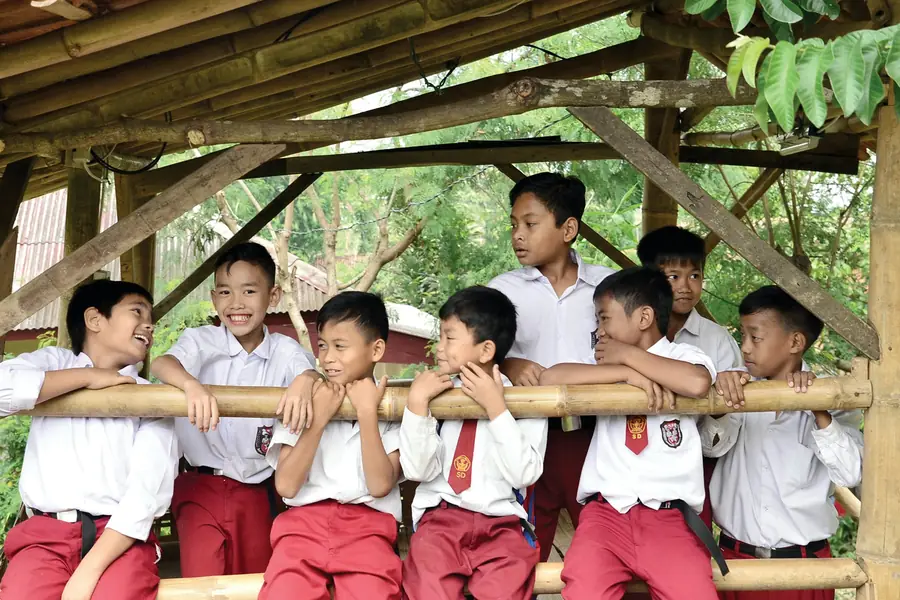 Schoolchildren in uniforms smiling on a bamboo bench